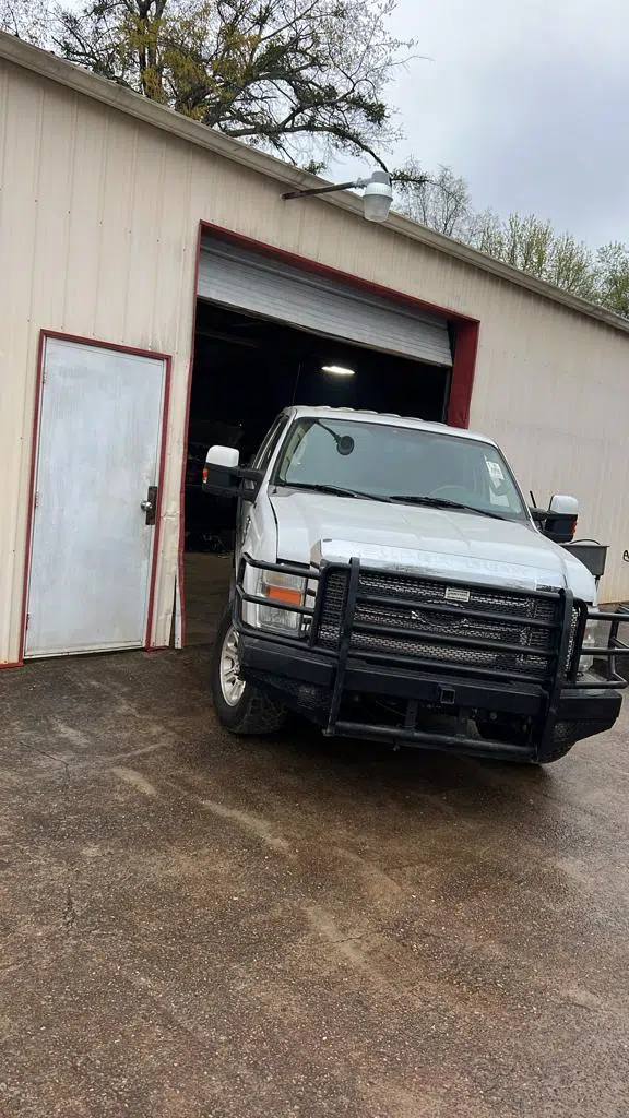 White pickup truck parked in front of an open shop bay door — PIQUET AUTO SERVICE in Greenville